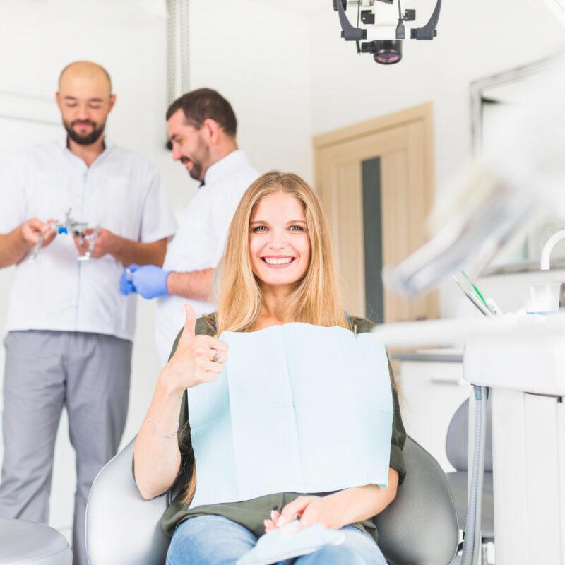 smiling female patient gesturing ok sign front two male dentist